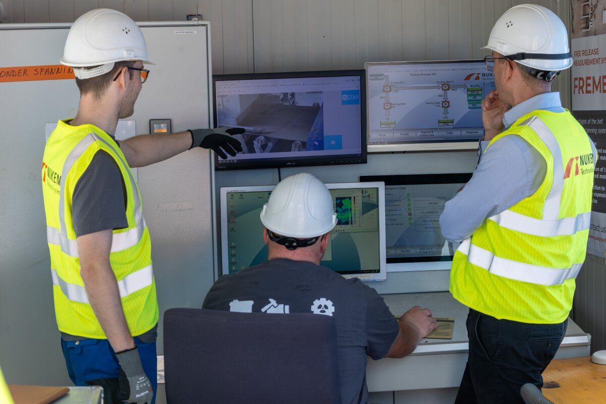 Auf einer Baustelle beraten sich Kollegen miteinander, während sie auf die Bildschirme vor sich schauen.